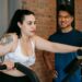 Exhausted young obese woman training on elliptical machine with support of Asian male instructor
